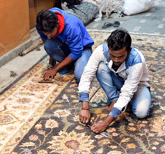 Des hommes indiens rasent un tapis de façon traditionelle.